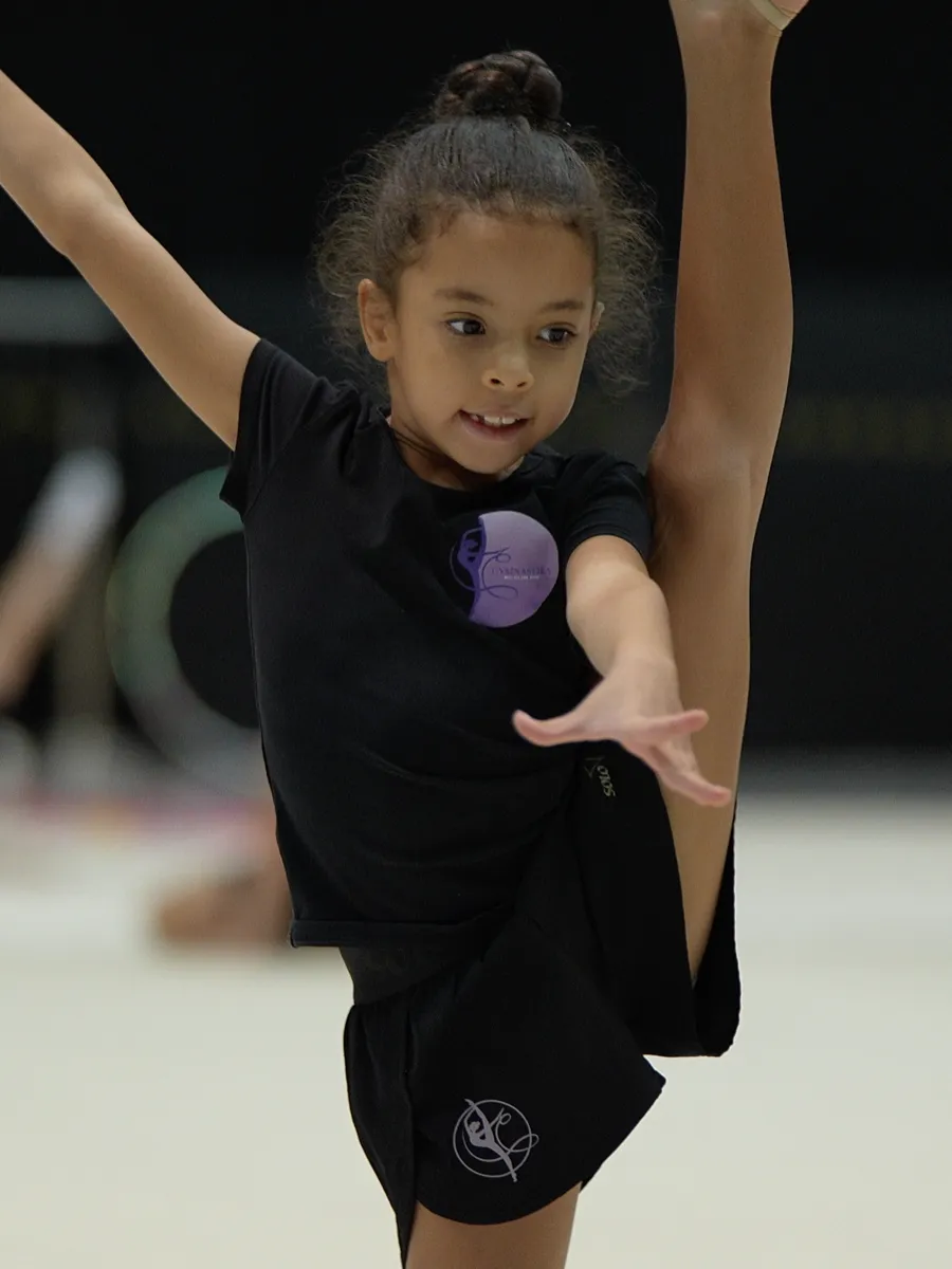 Юная гимнастка выполняет элемент на ковре в зале GYMNASTIKA